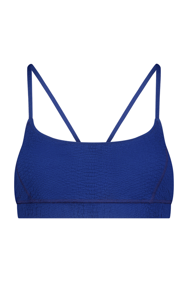 The Emery Bra by Gigi C Sport is a blue, minimalist bralette with thin straps and breathable, textured knit fabric, elegantly laid flat against a white background.