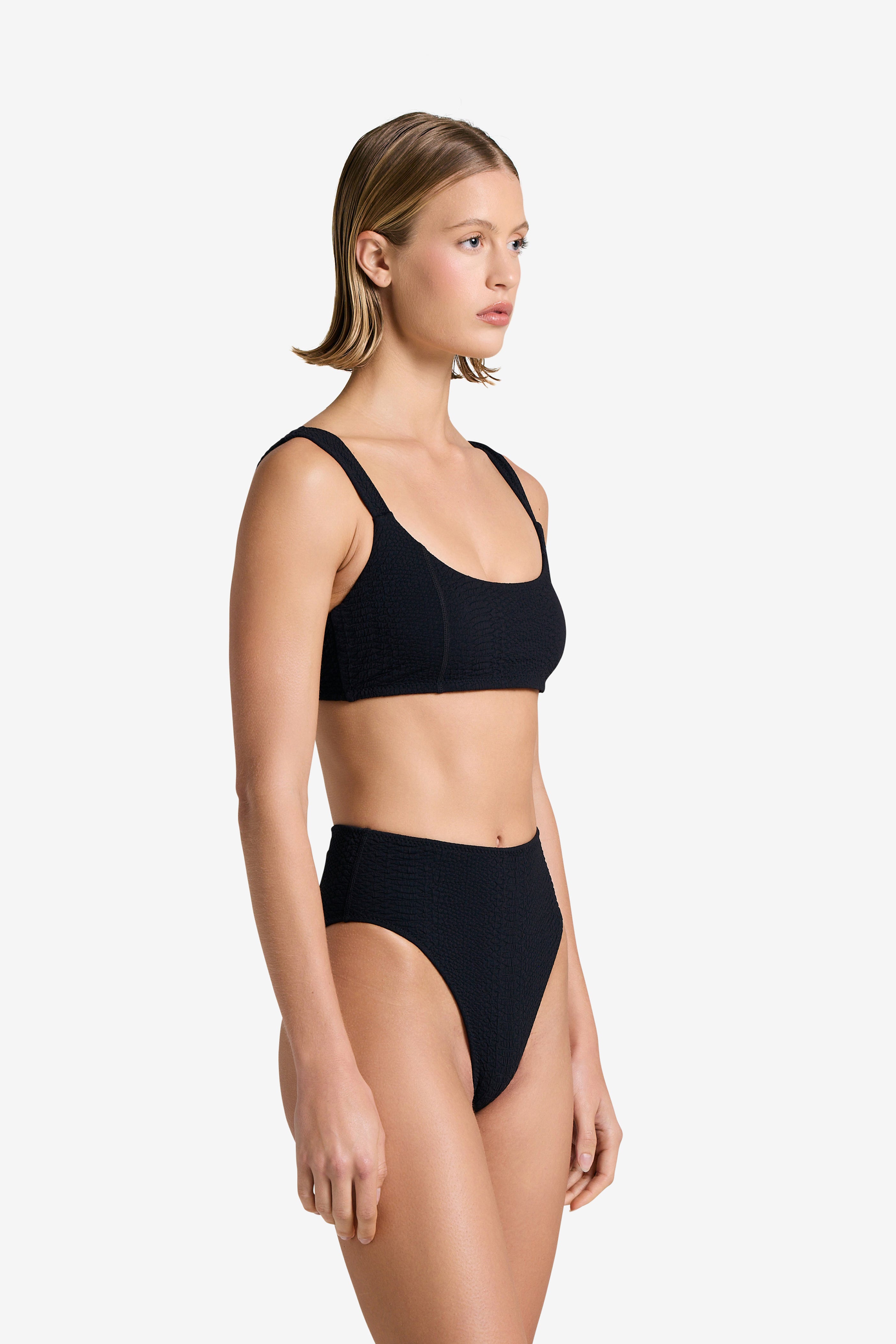 A person with short hair wearing a Dawson Top by Gigi C Bikinis poses against a plain white background, looking to the side. The stylish bikini features removable bust pads for customizable comfort.