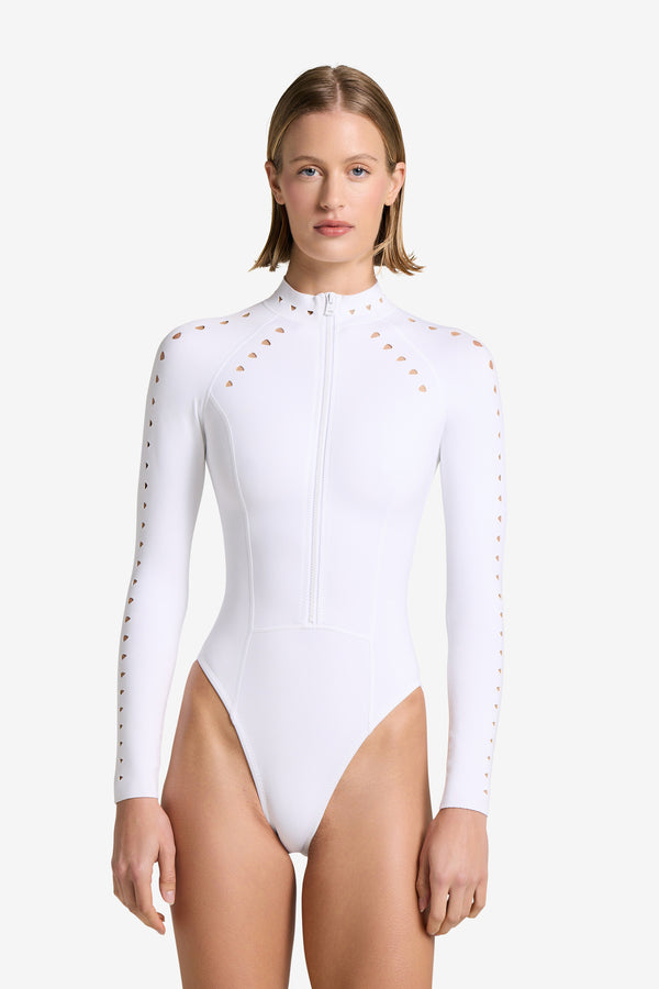 A person wears a sleek, form-fitting Riley Surfsuit Full Coverage by Gigi C Bikinis, featuring a front zipper and geometric cutout design on the shoulders and sleeves. Against a plain background, its modern style is highlighted by a high-cut leg for an effortlessly chic appearance.