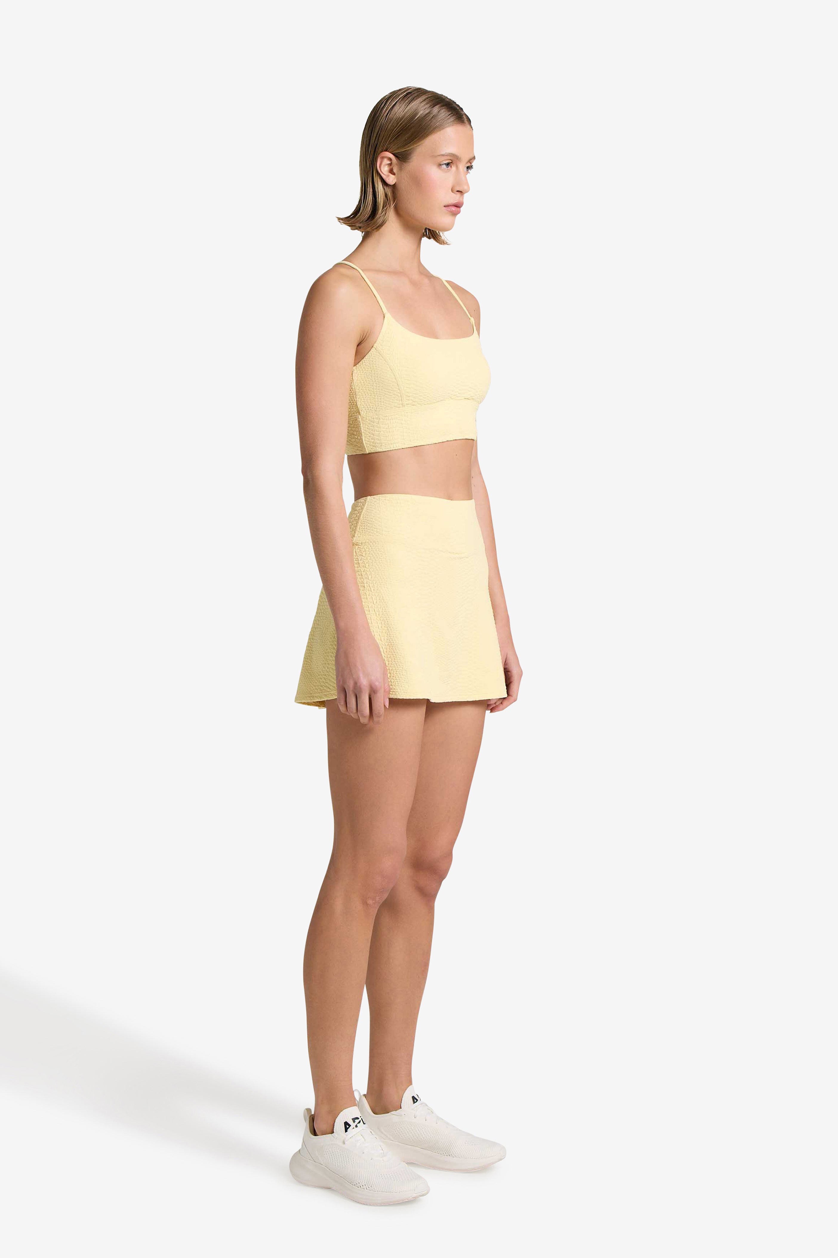 A person stands confidently in a Finle Bra from Gigi C Sport paired with the chic Heidi Skort and white sneakers against a plain white background.