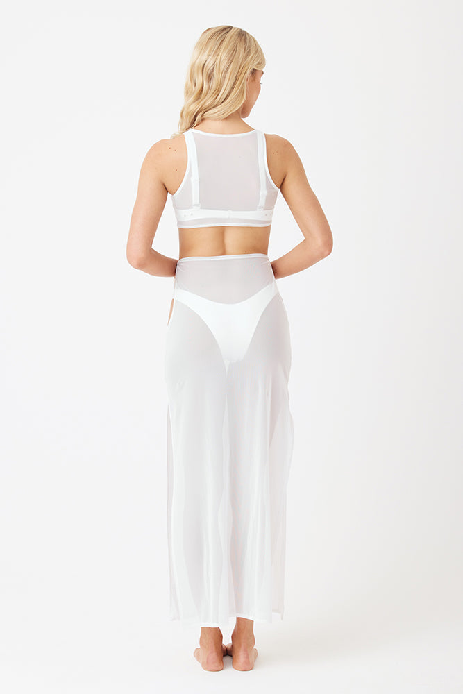 A person with long blonde hair faces away, wearing the Gigi C Bikinis Catherine Maxi Mesh Dress. This sleeveless, floor-length sheer outfit, with a fine mesh top and long skirt, reveals a bikini underneath against a plain white background for a minimalist look.