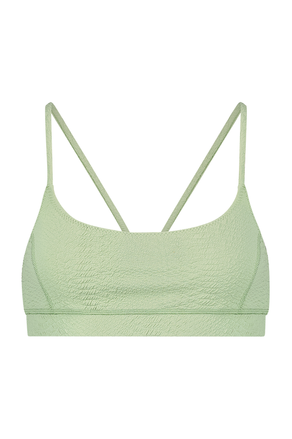 The Gigi C Sport Emery Bra is a light green, textured bralette with spaghetti straps, providing light support. Made from breathable knit fabric, it features a crinkled look and a simple design set against a solid black background.