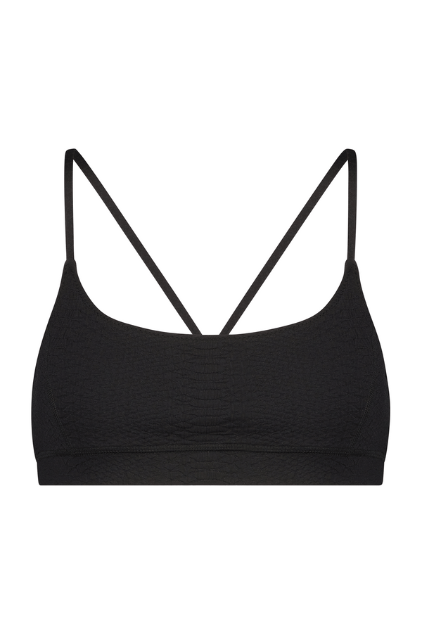 The Gigi C Sport Emery Bra, a black bralette with thin straps, is showcased on a white backdrop, featuring a subtle faux snakeskin texture that exudes simplicity and minimalist design.