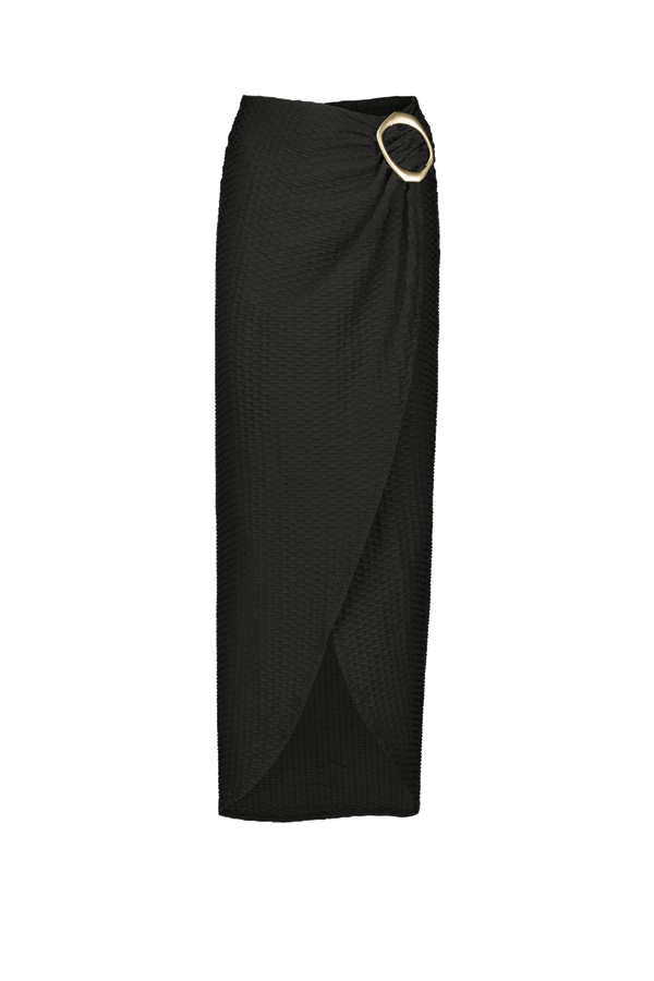 The Gigi C Bikinis Estelle Skirt is a long black wrap skirt with textured fabric, an asymmetrical hem, and a thigh-high split. It features a large gold oval buckle on the side that adds a cinched drape effect, elegantly complementing its gold finish.