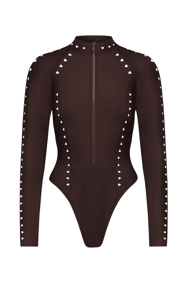 The Riley Surfsuit by Gigi C Bikinis is a long-sleeve brown bodysuit made from form-fitting scuba fabric, featuring a front zip closure and triangular white studs on the arms and sides that form an elegant geometric pattern.