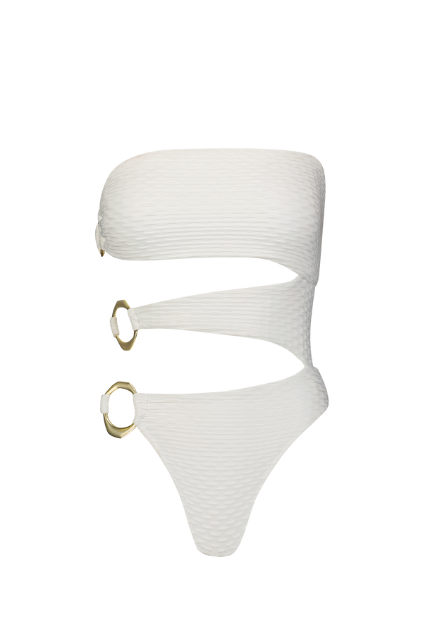 The Sami One Piece by Gigi C Bikinis is a white swimsuit with a ribbed texture and luxurious feel. It features a wraparound design with two large asymmetric brushed gold rings on the side, while its strapless top offers a bold, modern look against a black background.