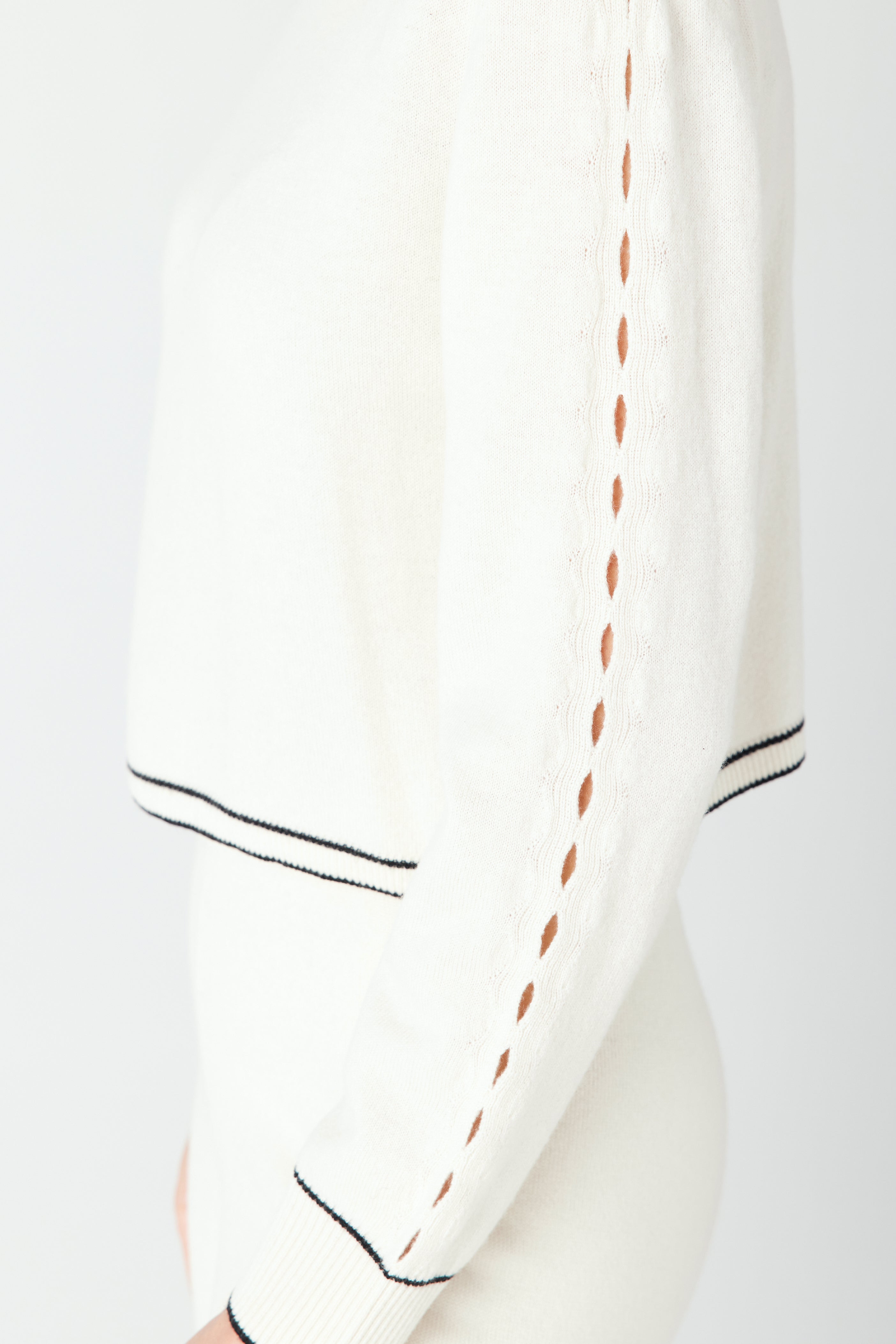 Side view close-up of someone wearing the Jacqueline Pullover by Gigi C Lounge, featuring a white recycled cashmere sweater with black trim and teardrop cut-out detailing on the sleeve.