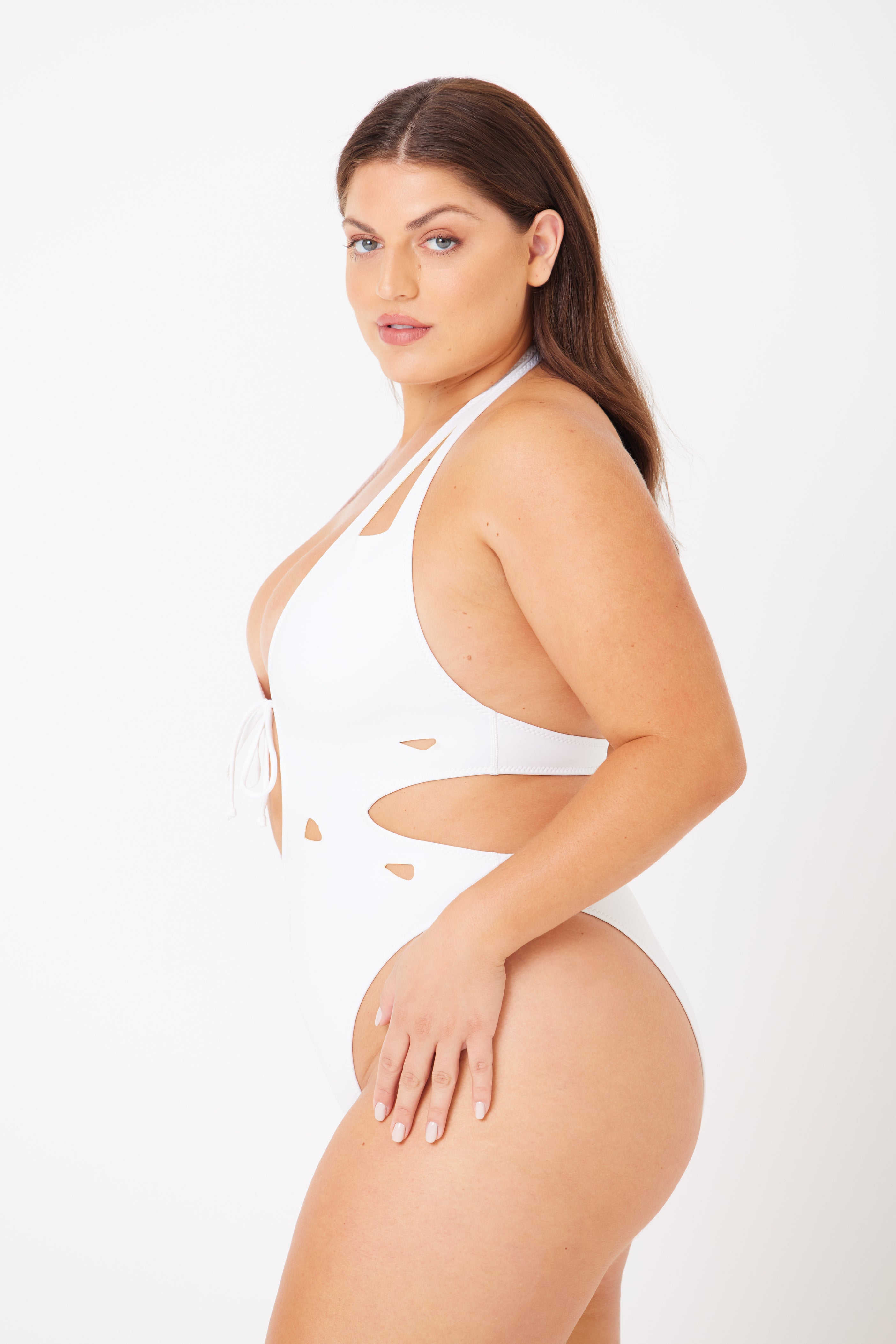 Wearing the Charlie Plunging One-Piece by Gigi C Bikinis, a woman with long brown hair and neutral makeup poses confidently against a white background.