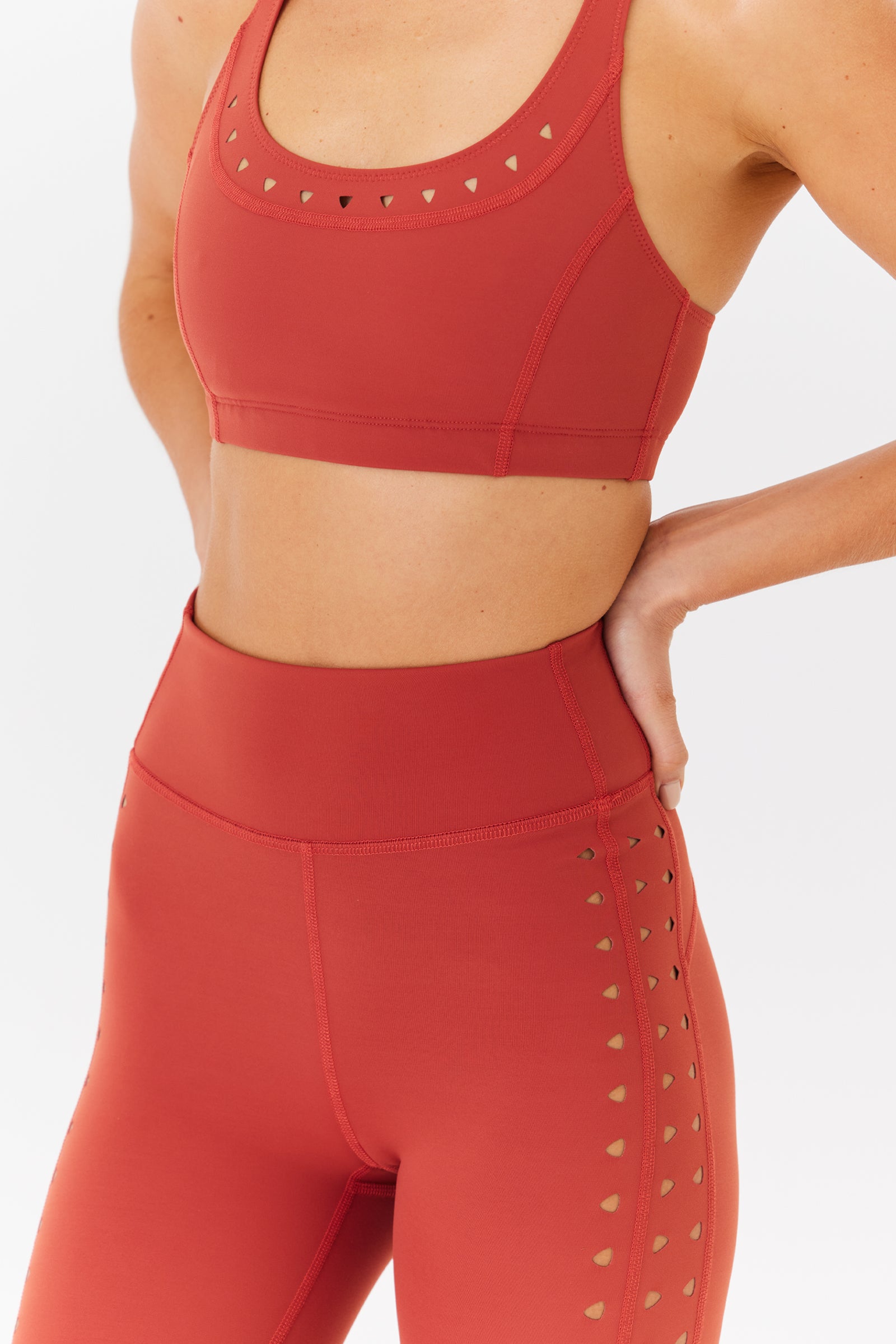 Person in a red Annabelle Bra Top by Gigi C Sport with removable pads, paired with high-waisted leggings featuring heart-shaped cutouts, stands with one hand on their hip against a plain white background.